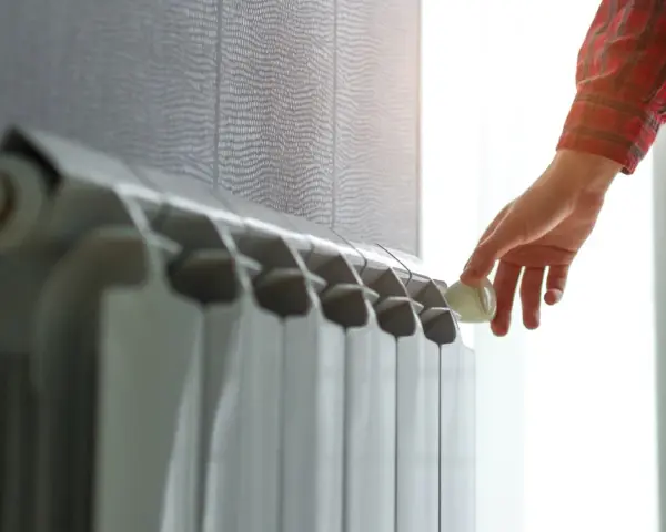 Mano che regola la valvola di un termosifone. Scopri quanto costa cambiare i termosifoni per un riscaldamento efficiente.