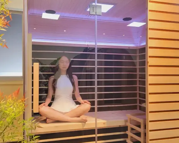Donna in meditazione in una sauna a infrarossi, un luogo di pace dove ci si chiede perché non sudo in sauna.
