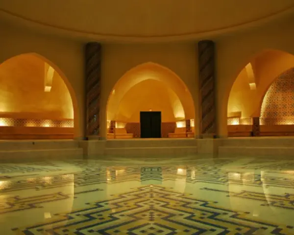 Interno di un bagno dei turchi con piscina e mosaici geometrici. Archi moreschi e colonne decorate creano un'atmosfera orientale.