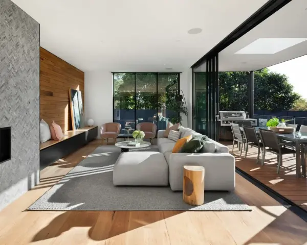 Soggiorno moderno con camino in pietra, divano bianco, e un bellissimo parquet essenze che si estende verso l'esterno, collegandosi alla zona pranzo esterna.