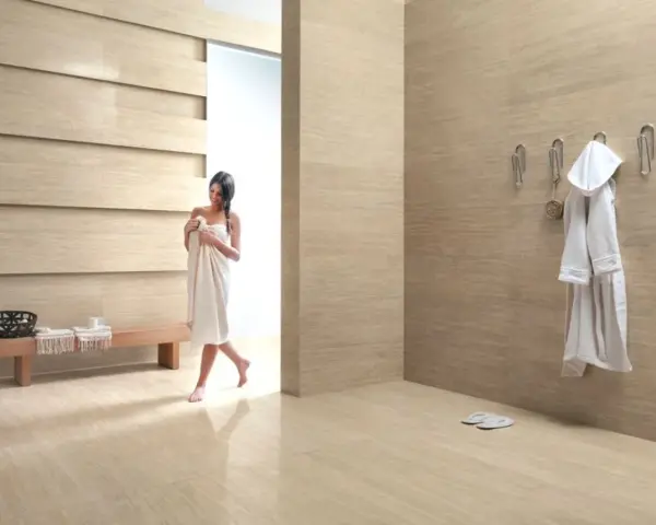 Bagni moderni con donna avvolta in un asciugamano, accappatoio appeso e panchina in legno.