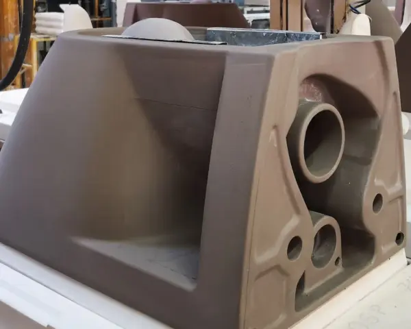 A brown ceramic toilet tank mold with visible pipes and openings, in a workshop setting.