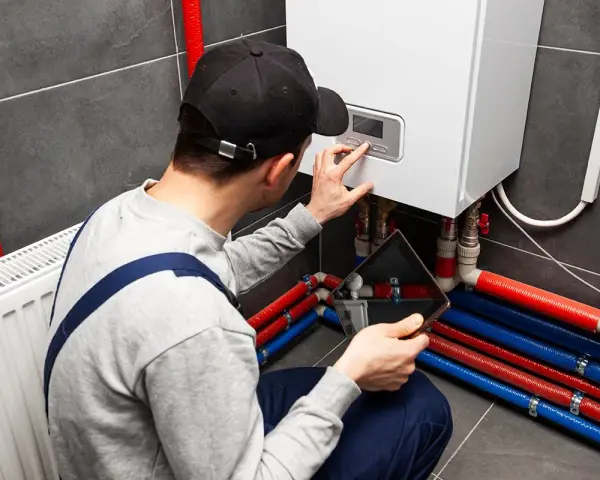 Uomo con tablet e cappellino esegue pulizia impianto riscaldamento fai da te, controllando la caldaia e i tubi colorati.