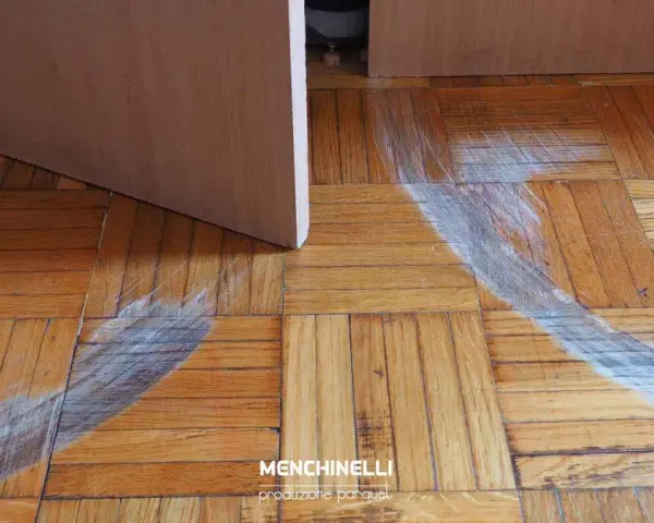 Rimozione di parquet incollato con segni di usura sul pavimento in legno.
