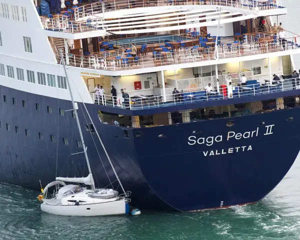 Una piccola barca a vela si trova in una **posa a tolda di nave irregolare** accanto alla massiccia nave da crociera "Saga Pearl II".