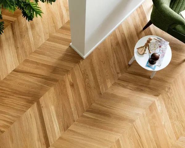 Un elegante parquet oliato a spina di pesce, con un tavolino bianco e una poltrona verde. Scopri come pulire il tuo parquet oliato per mantenerlo splendente.