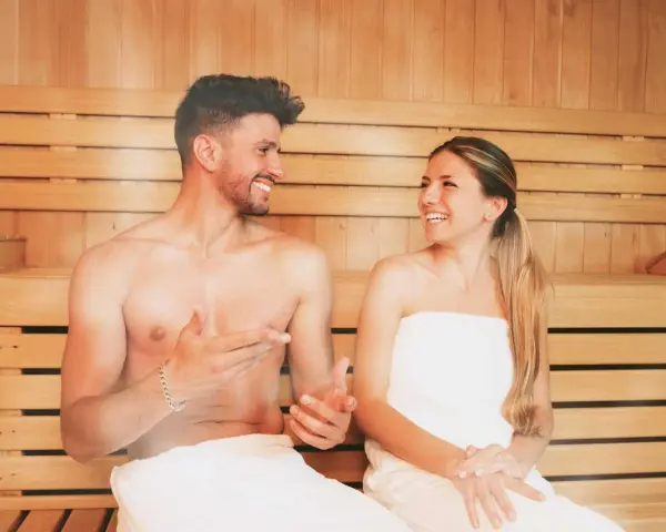Coppia sorridente in una sauna di legno, un rituale di benessere quotidiano.