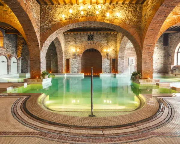 Un suggestivo thermarium, con vasche termali verdi sotto archi in mattoni e pietra, evoca un'atmosfera di antico benessere.