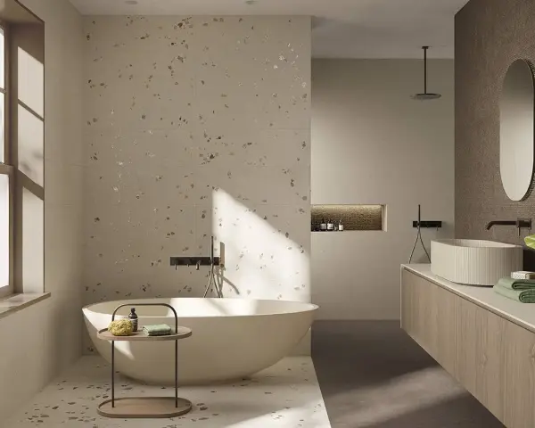 Bagno moderno con vasca freestanding e lavabo su mobile in legno. Il pavimento fap, con le sue venature chiare e inclusioni dorate, riflette la luce naturale.