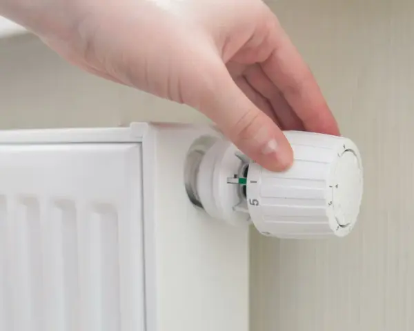 Mano che regola la manopola di un termosifone per ottimizzare la potenza.