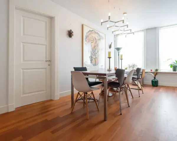 Un elegante soggiorno con parquet doussié e arredamento moderno. Tavolo da pranzo con sedie di design, quadro astratto e lampadario geometrico.