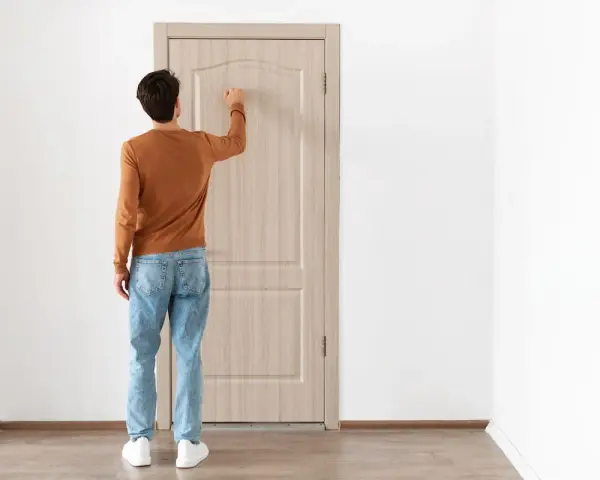 Uomo con maglione arancione e jeans bussa alla porta, forse per alzare la porta per posa pavimento.