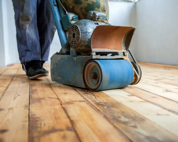 Levigatura parquet: un operaio usa una levigatrice per preparare il pavimento prima dell'imbiancatura. Il legno grezzo risplende sotto la macchina.
