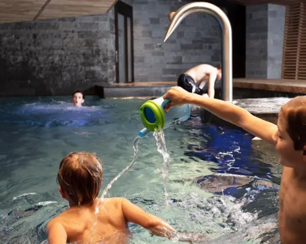 Bambini giocano in piscina, con un annaffiatoio. Nessuna indicazione su sauna età minima.