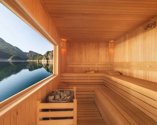 Interno di una sauna in legno con vista su un lago e montagne. Un luogo perfetto per capire cos'è una spa: relax e natura.