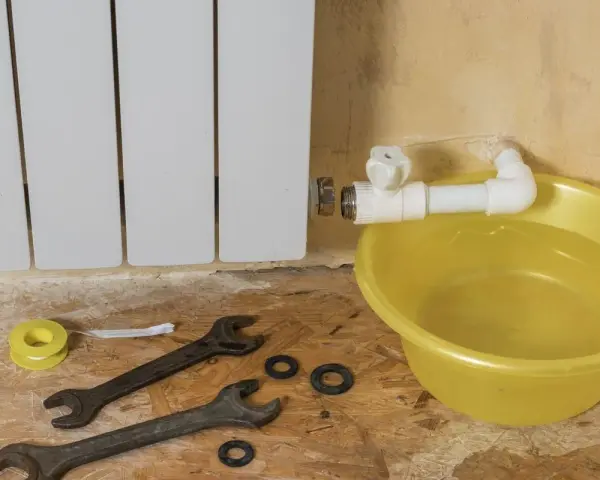 Riparazione di un termosifone che perde acqua e presenta ruggine. Attrezzi e bacinella gialla pronti per l'intervento.