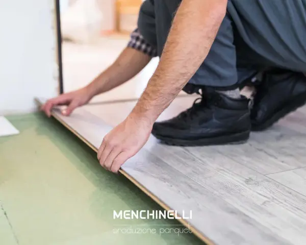 Installazione di un parquet flottante con finitura effetto legno chiaro. Un artigiano posa le tavole con cura.
