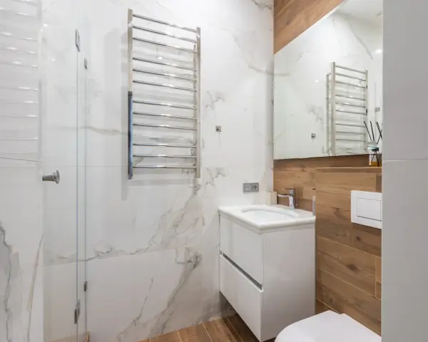 Bagno moderno con termoarredi cromati, lavabo sospeso e rivestimenti in marmo e legno.