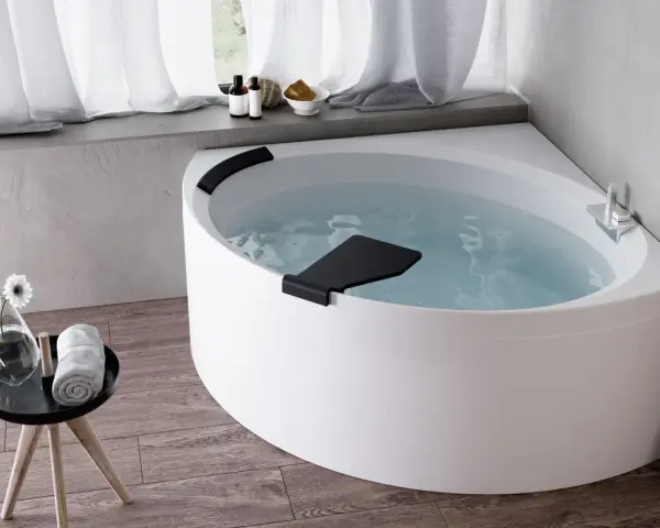 Una vasca da bagno angolare bianca, piena d'acqua, con accessori da bagno e un fiore su un tavolino. Un'esperienza novellini divina.