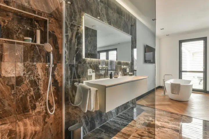 Bagno di lusso con doccia e vasca. Rubinetteria Bossini cromata, lavabo sospeso e specchio illuminato. Marmo scuro e parquet.