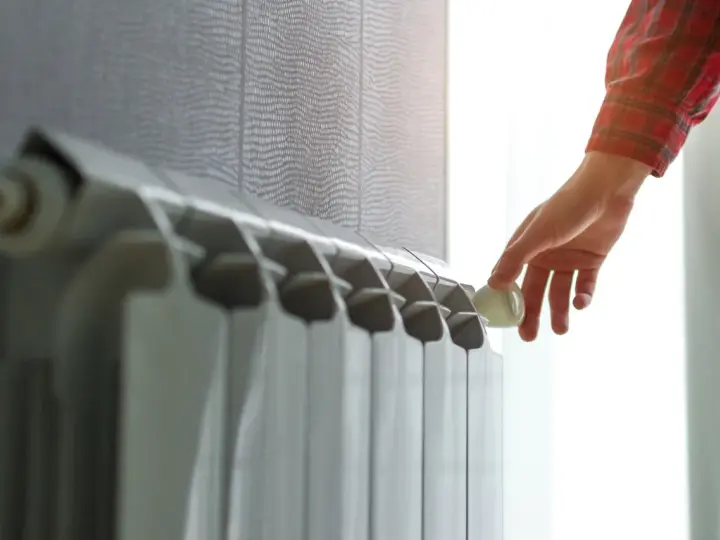 Mano che regola la valvola di un termosifone. Scopri quanto costa cambiare i termosifoni per un riscaldamento efficiente.
