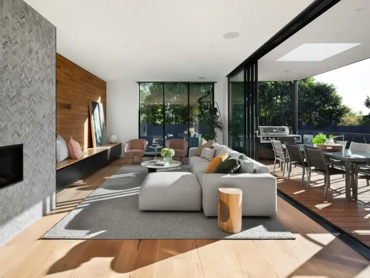 Soggiorno moderno con camino in pietra, divano bianco, e un bellissimo parquet essenze che si estende verso l'esterno, collegandosi alla zona pranzo esterna.