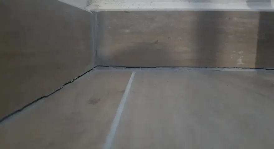 Angolo di una stanza con pavimento in legno e battiscopa. Si vedono le crepe tra il battiscopa e il muro, un dettaglio da considerare dopo il massetto.
