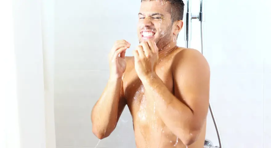 Uomo sotto la doccia dopo allenamento, con acqua che gli scorre sul viso e sul corpo.