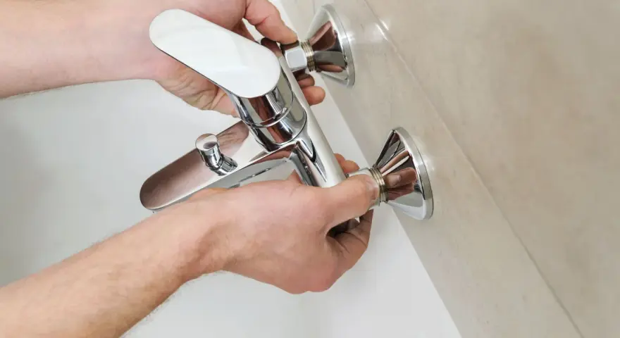 Mani che installano un nuovo miscelatore cromato per la vasca da bagno, parte della sostituzione miscelatore vasca da bagno.