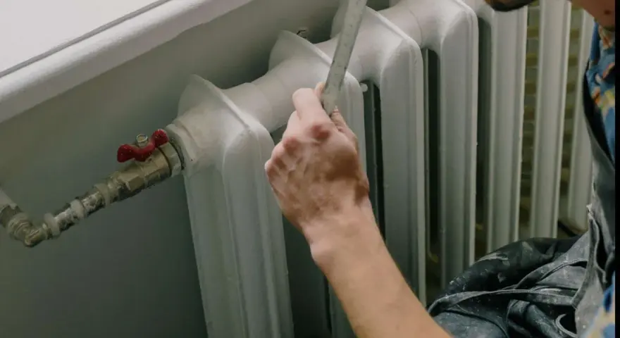 Mano con righello vicino a termosifone, pronto a cambiare valvola termostatica senza svuotare impianto.