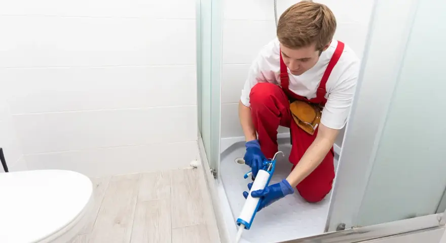 Un operaio con tuta rossa sigilla la fuga tra piatto doccia e piastrelle, prevenendo infiltrazioni d'acqua.