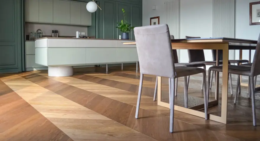 Un elegante parquet a spina di pesce crea un disegno dinamico sotto un tavolo da pranzo e una moderna cucina verde.