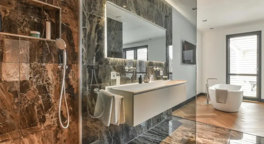 Bagno di lusso con doccia e vasca. Rubinetteria Bossini cromata, lavabo sospeso e specchio illuminato. Marmo scuro e parquet.