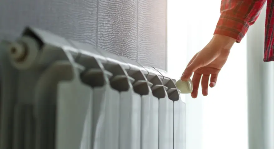 Mano che regola la valvola di un termosifone. Scopri quanto costa cambiare i termosifoni per un riscaldamento efficiente.