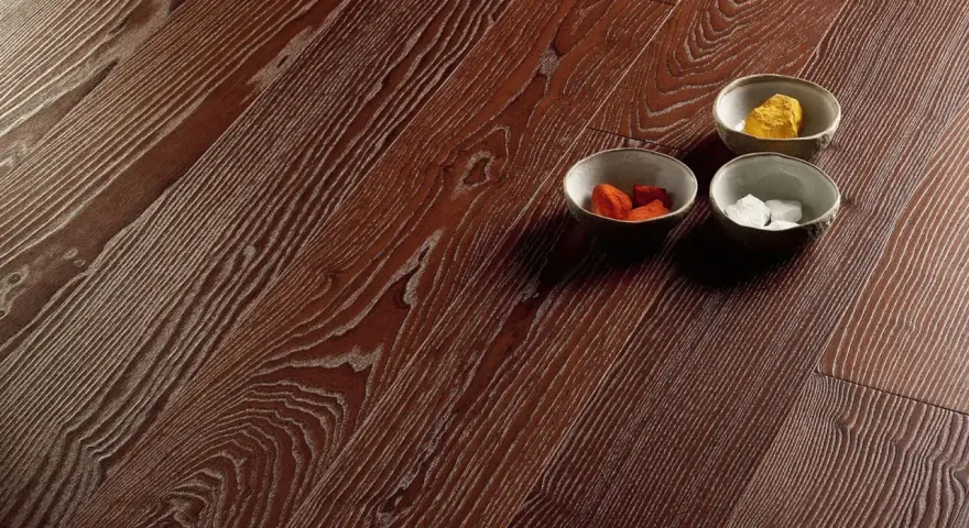 Superficie in parquet massello o prefinito con venature marcate. Tre ciotoline con elementi decorativi colorati.