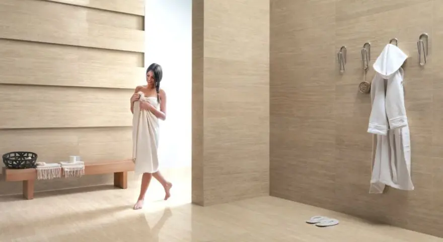 Bagni moderni con donna avvolta in un asciugamano, accappatoio appeso e panchina in legno.