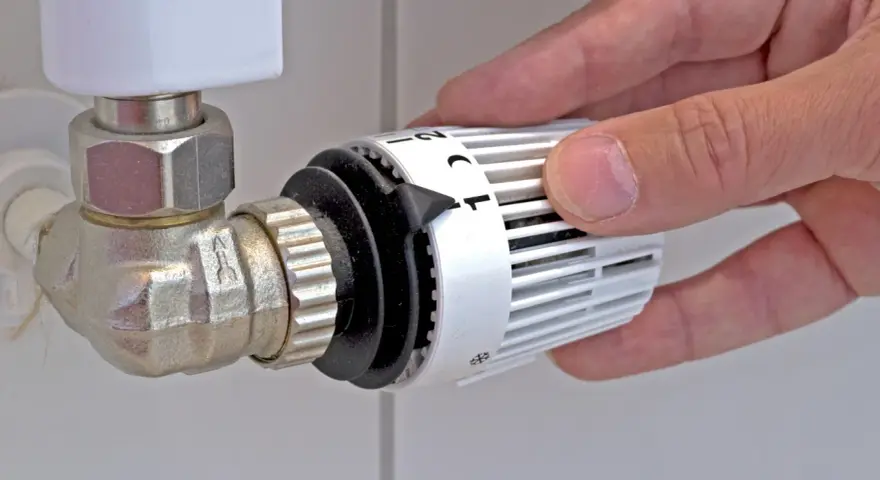 Mano che regola la manopola del termostato per misurare la temperatura dei termosifoni.