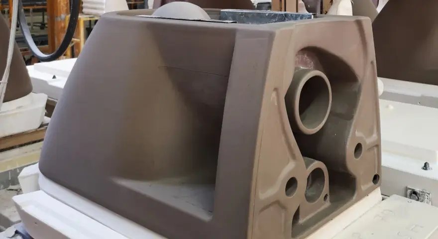 A brown ceramic toilet tank mold with visible pipes and openings, in a workshop setting.