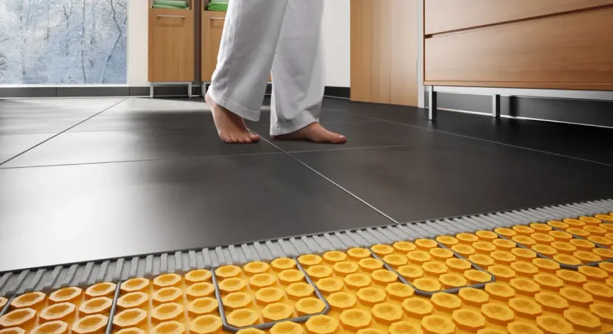Piedi nudi su pavimento scuro, con sistema di riscaldamento a pavimento su pavimento esistente visibile sotto.