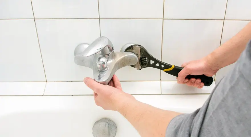 Mano con chiave inglese ripara un rubinetto che perde dal miscelatore, sopra la vasca da bagno.