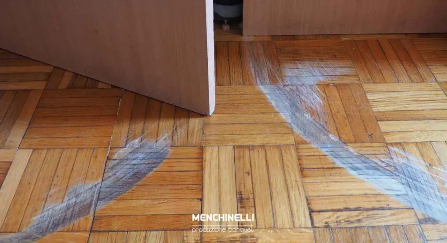 Rimozione di parquet incollato con segni di usura sul pavimento in legno.