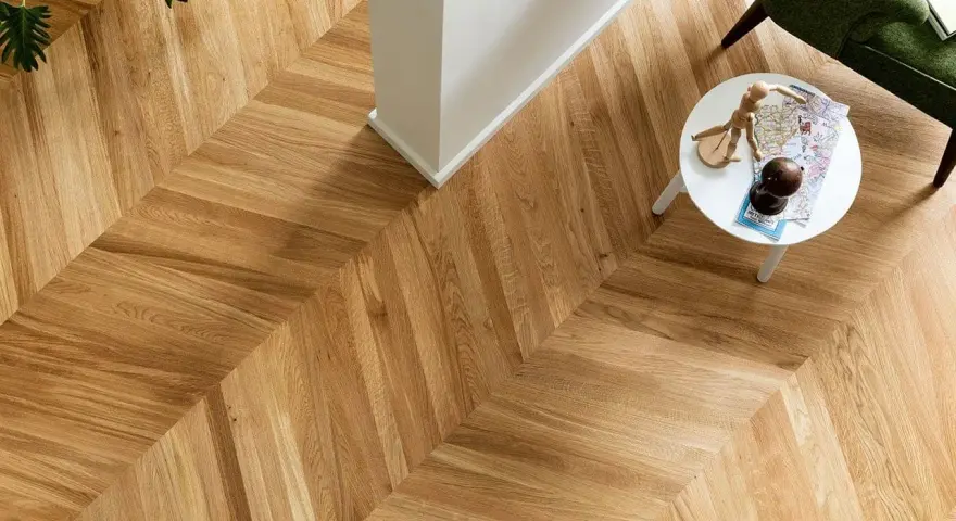 Un elegante parquet oliato a spina di pesce, con un tavolino bianco e una poltrona verde. Scopri come pulire il tuo parquet oliato per mantenerlo splendente.