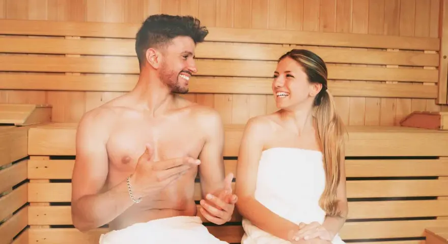 Coppia sorridente in una sauna di legno, un rituale di benessere quotidiano.