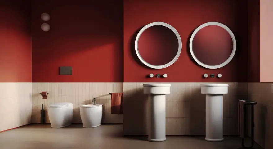 Bagno moderno con wc, bidet e due lavabi a colonna. L'artceramica bianca risalta sulle pareti rosse e le piastrelle chiare.