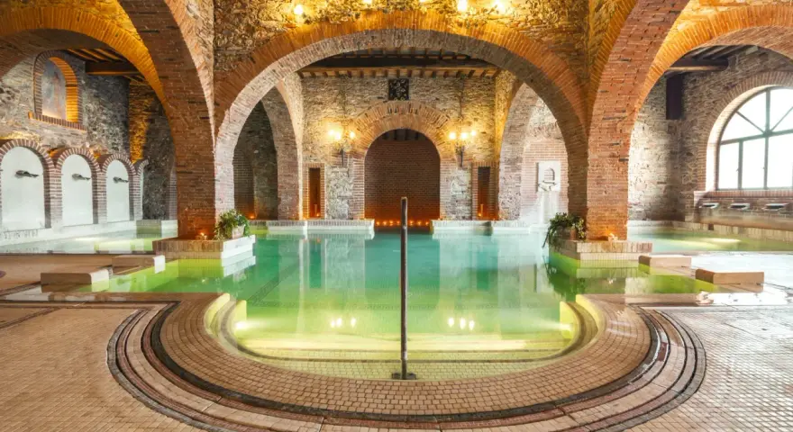 Un suggestivo thermarium, con vasche termali verdi sotto archi in mattoni e pietra, evoca un'atmosfera di antico benessere.