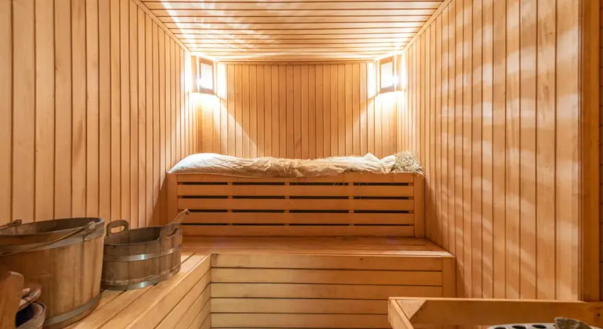 Interno di una sauna norvegese in legno, con panche, secchi e luci soffuse.