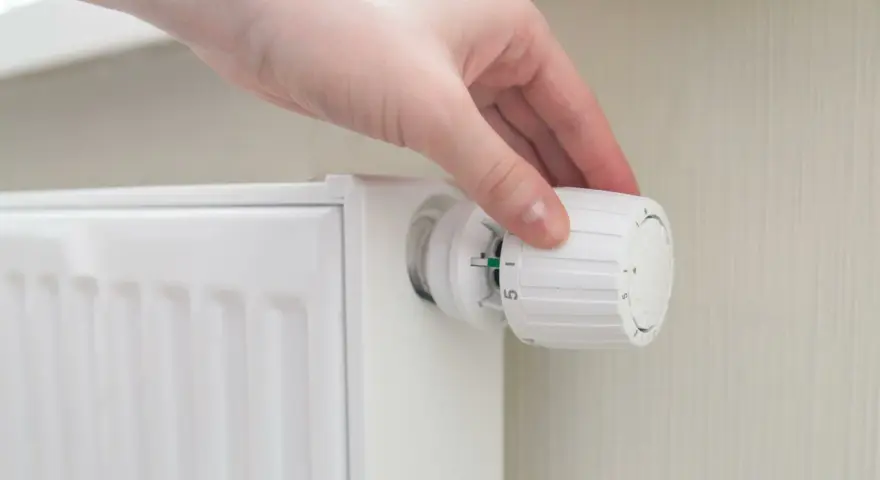 Mano che regola la manopola di un termosifone per ottimizzare la potenza.