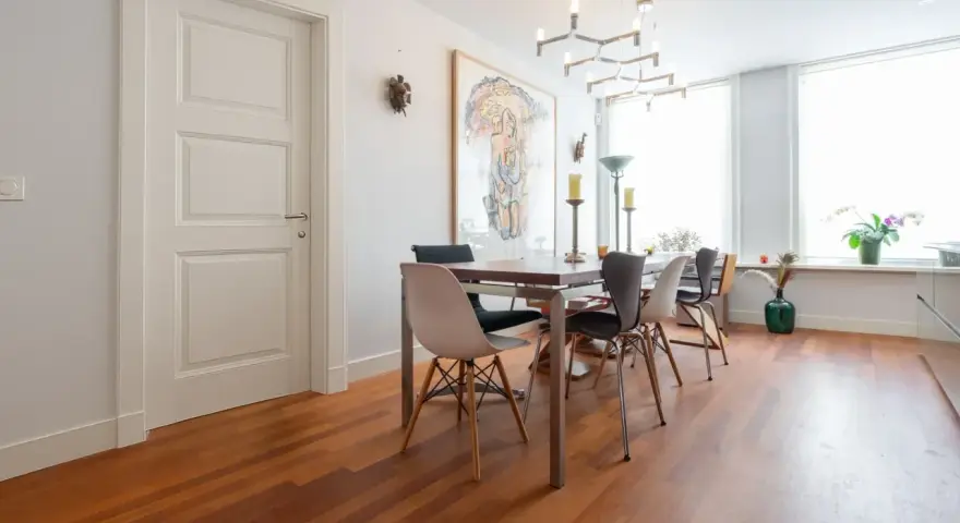 Un elegante soggiorno con parquet doussié e arredamento moderno. Tavolo da pranzo con sedie di design, quadro astratto e lampadario geometrico.