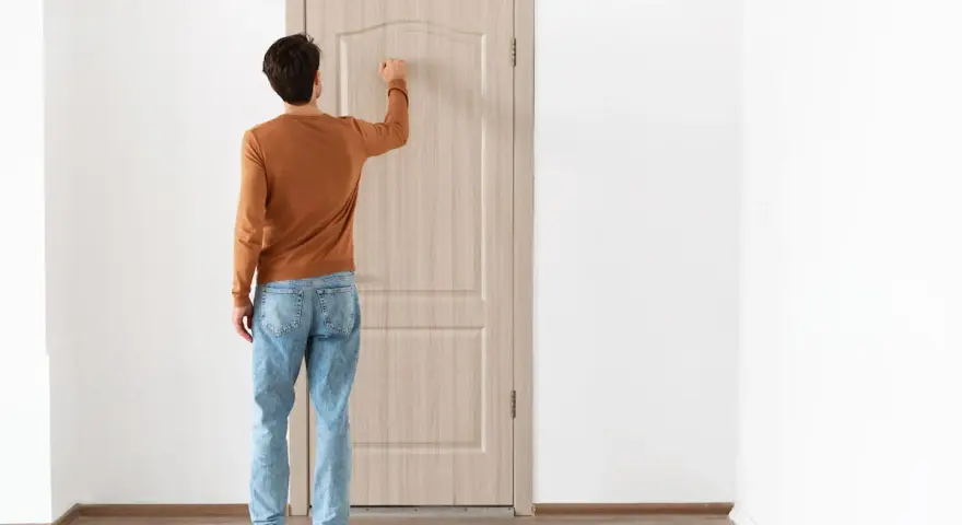 Uomo con maglione arancione e jeans bussa alla porta, forse per alzare la porta per posa pavimento.