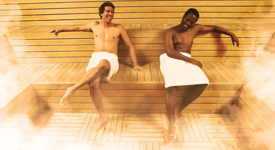 Due uomini sorridono nella sauna, godendosi il calore e il vapore. La sauna può offrire benefici per la pelle, inclusi quelli per la cellulite.